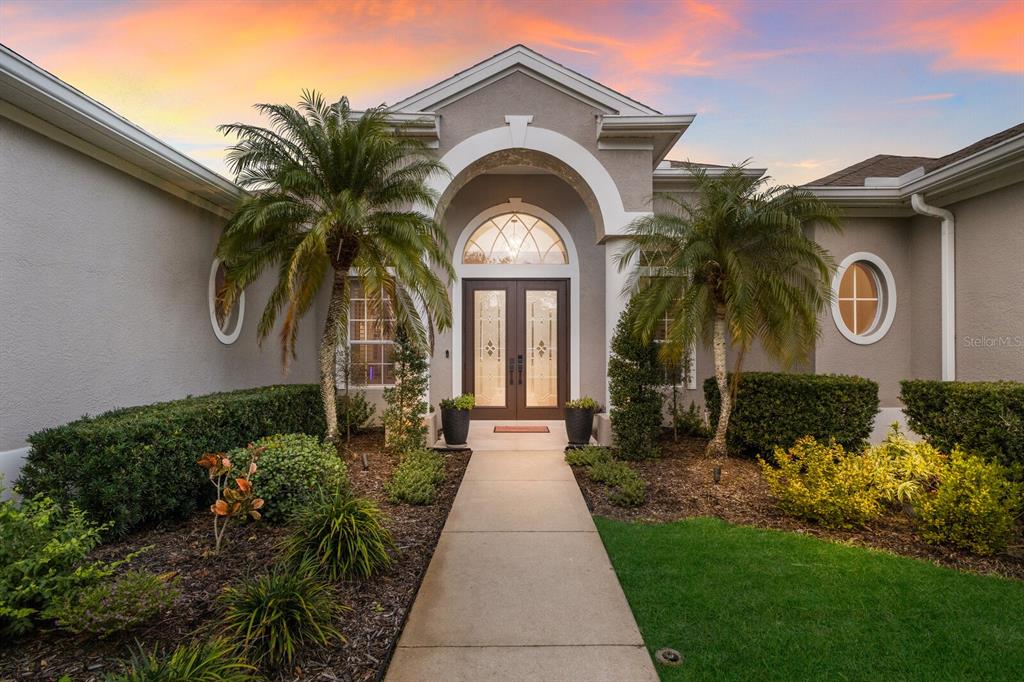 A concrete walkway leads to the arched entryway of a gray house with two palm trees — 9405 BOXTHORN PLACE, BRADENTON, FL