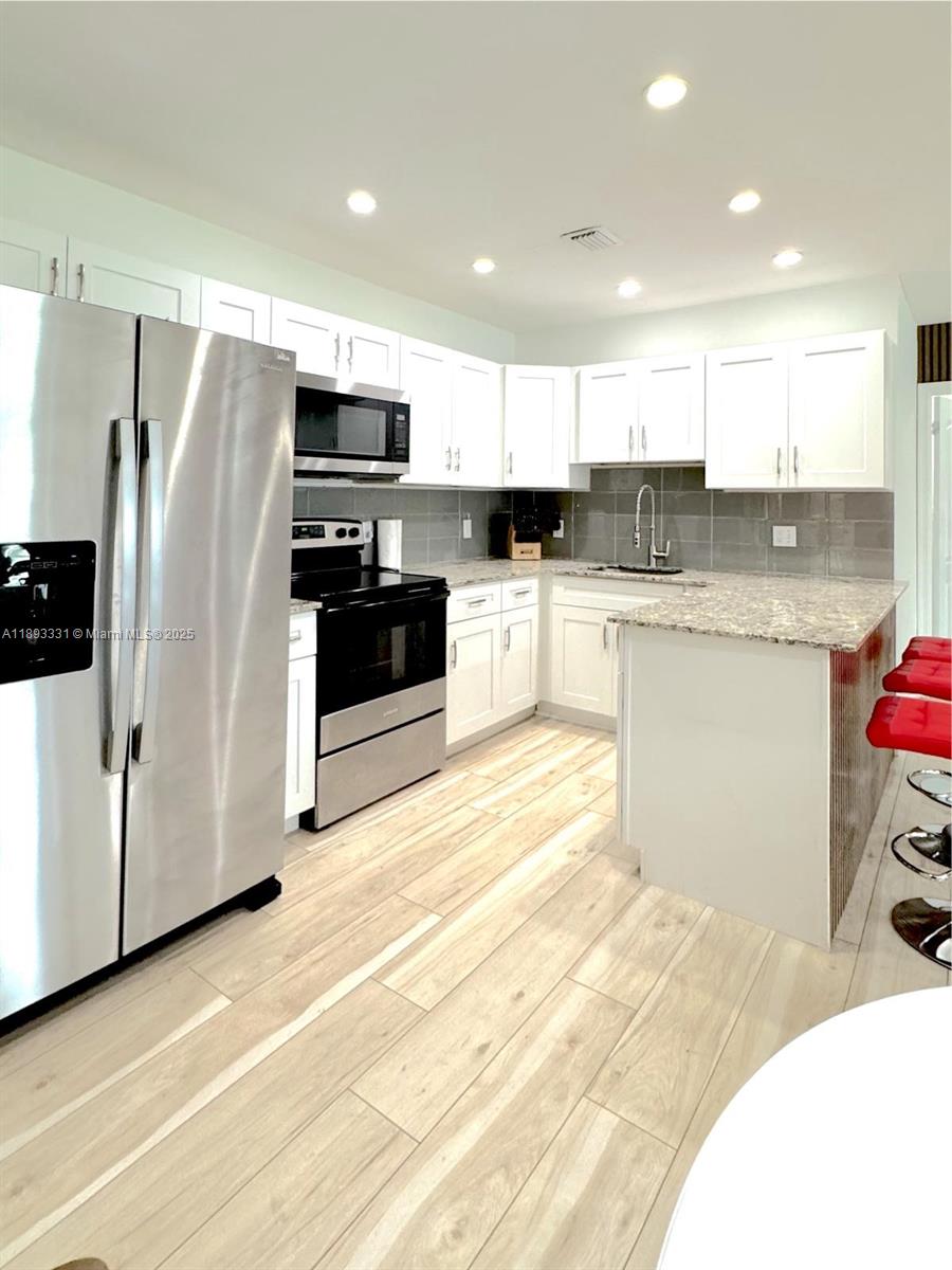 A kitchen features white cabinets, stainless steel appliances, granite countertops, and light wood-look flooring — 120 NE 9th Ave # 120A, Deerfield Beach FL 33441, DEERFIELD BEACH, FL