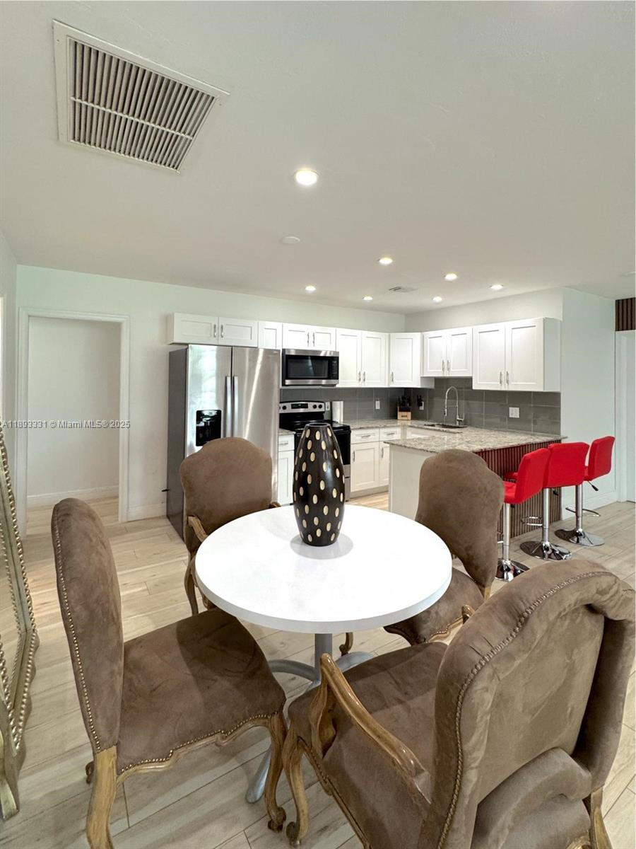 A kitchen features white cabinetry, granite countertops, stainless steel appliances, and a small dining area — 120 NE 9th Ave # 120A, Deerfield Beach FL 33441, DEERFIELD BEACH, FL