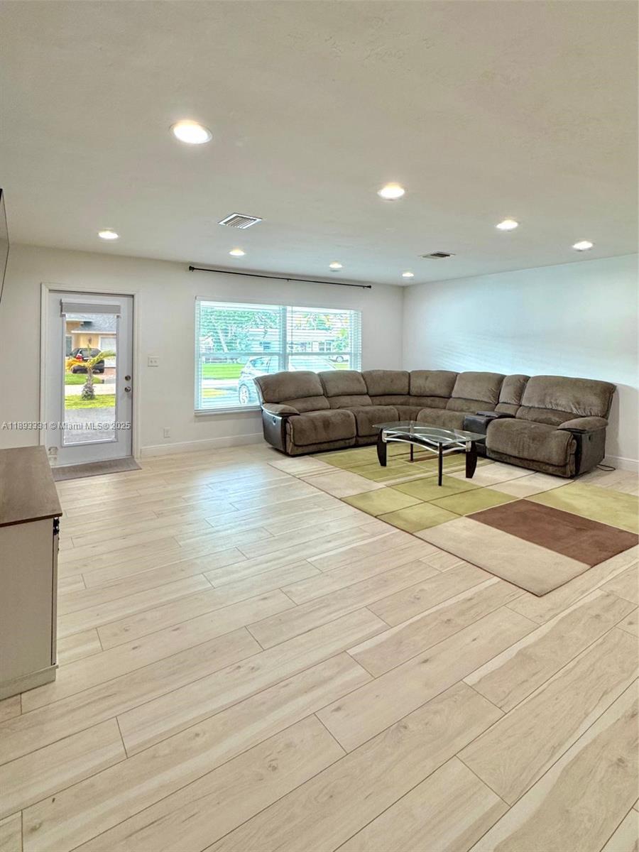 A living room features light wood-look tile flooring, recessed lighting, and a large sectional sofa — 120 NE 9th Ave # 120A, Deerfield Beach FL 33441, DEERFIELD BEACH, FL