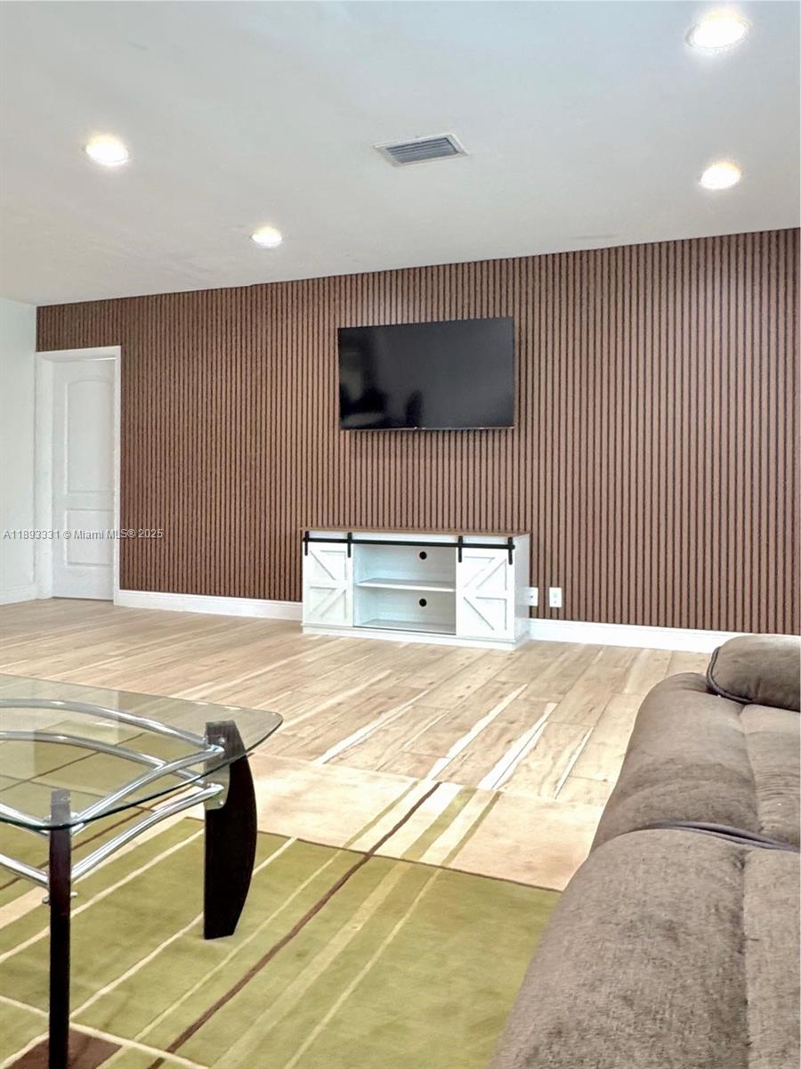 A living room features a wood-slat accent wall, a wall-mounted television, and a white media console — 120 NE 9th Ave # 120A, Deerfield Beach FL 33441, DEERFIELD BEACH, FL