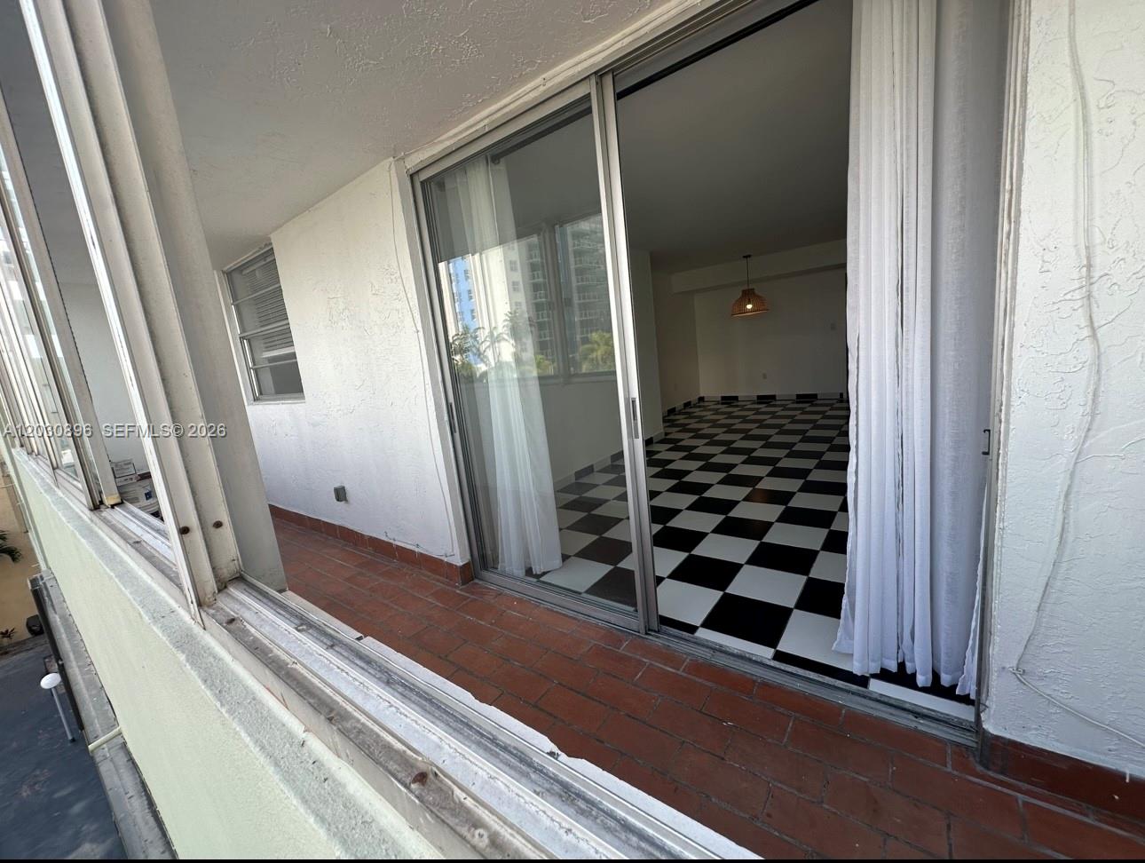 A balcony with red brick flooring overlooks a room featuring black and white checkered tile — 5055 NW 7th St # 409, Miami FL 33126, MIAMI, FL