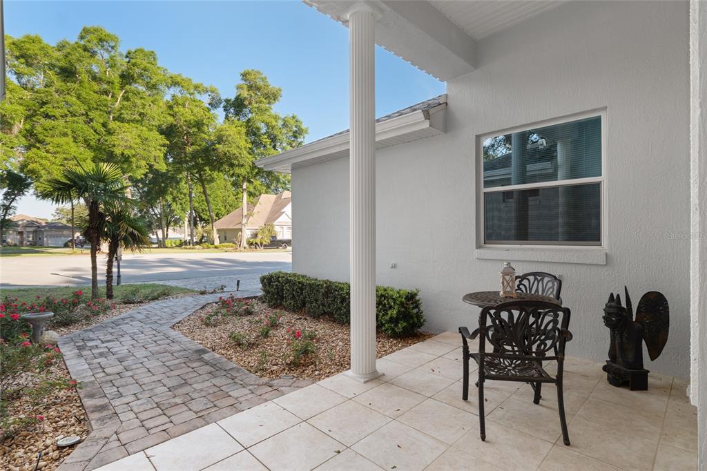 A paved walkway leads to a covered patio with a white column and metal furniture — 10801 SW 71ST AVE, OCALA, FL