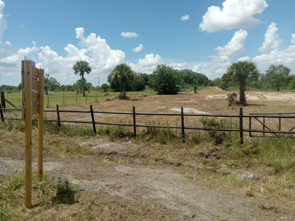 A fenced, cleared dirt lot features several palm trees under a bright, cloudy blue sky — 19145 NW 270th Street, Okeechobee FL 34972, OKEECHOBEE, FL