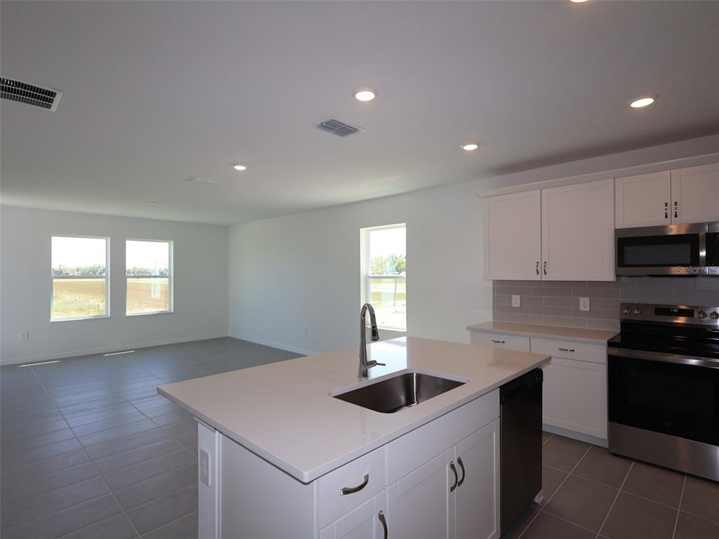 A kitchen with a central island, white cabinetry, and tile flooring overlooks an open living area — 9014 OPTIMIST WAY, PALMETTO, FL