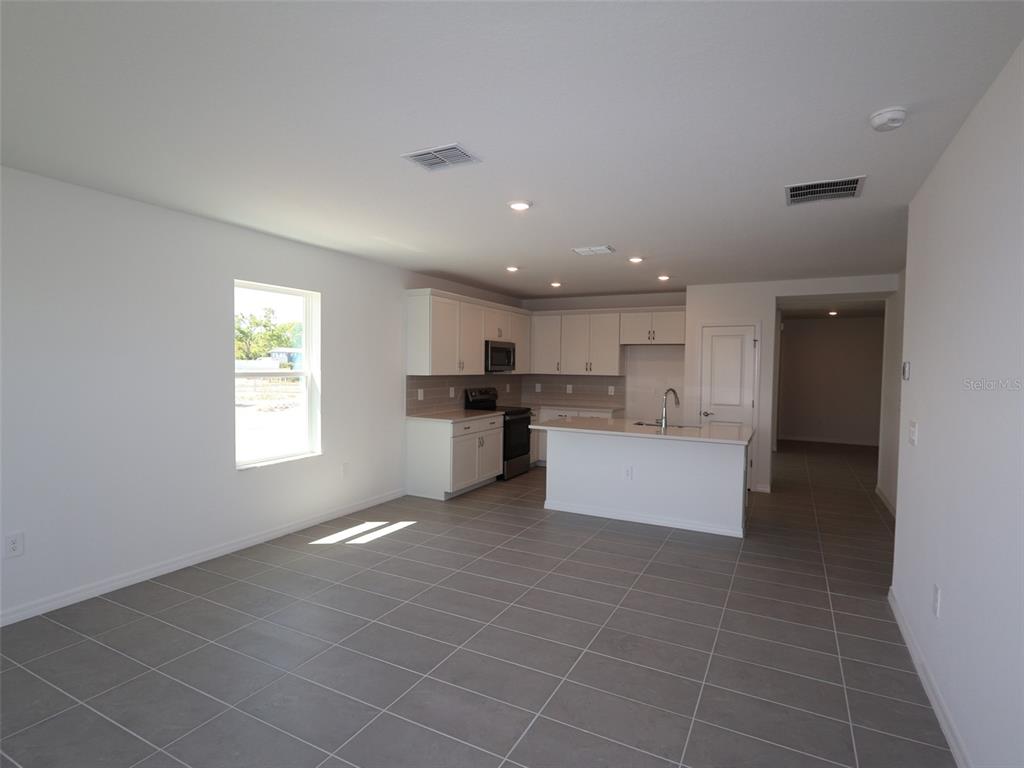An open-concept kitchen features white cabinets, stainless steel appliances, and gray tile flooring — 9014 OPTIMIST WAY, PALMETTO, FL