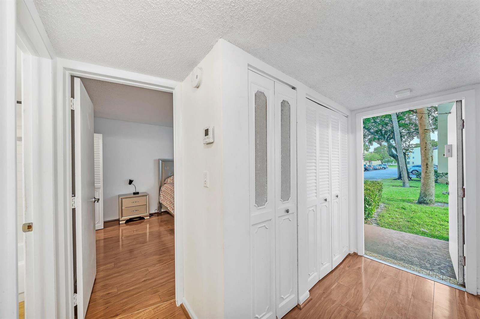 An entryway with wood-look flooring, white louvered closet doors, and a view of a bedroom — 5940 NW 64th Avenue Unit 101, Tamarac FL 33319, TAMARAC, FL