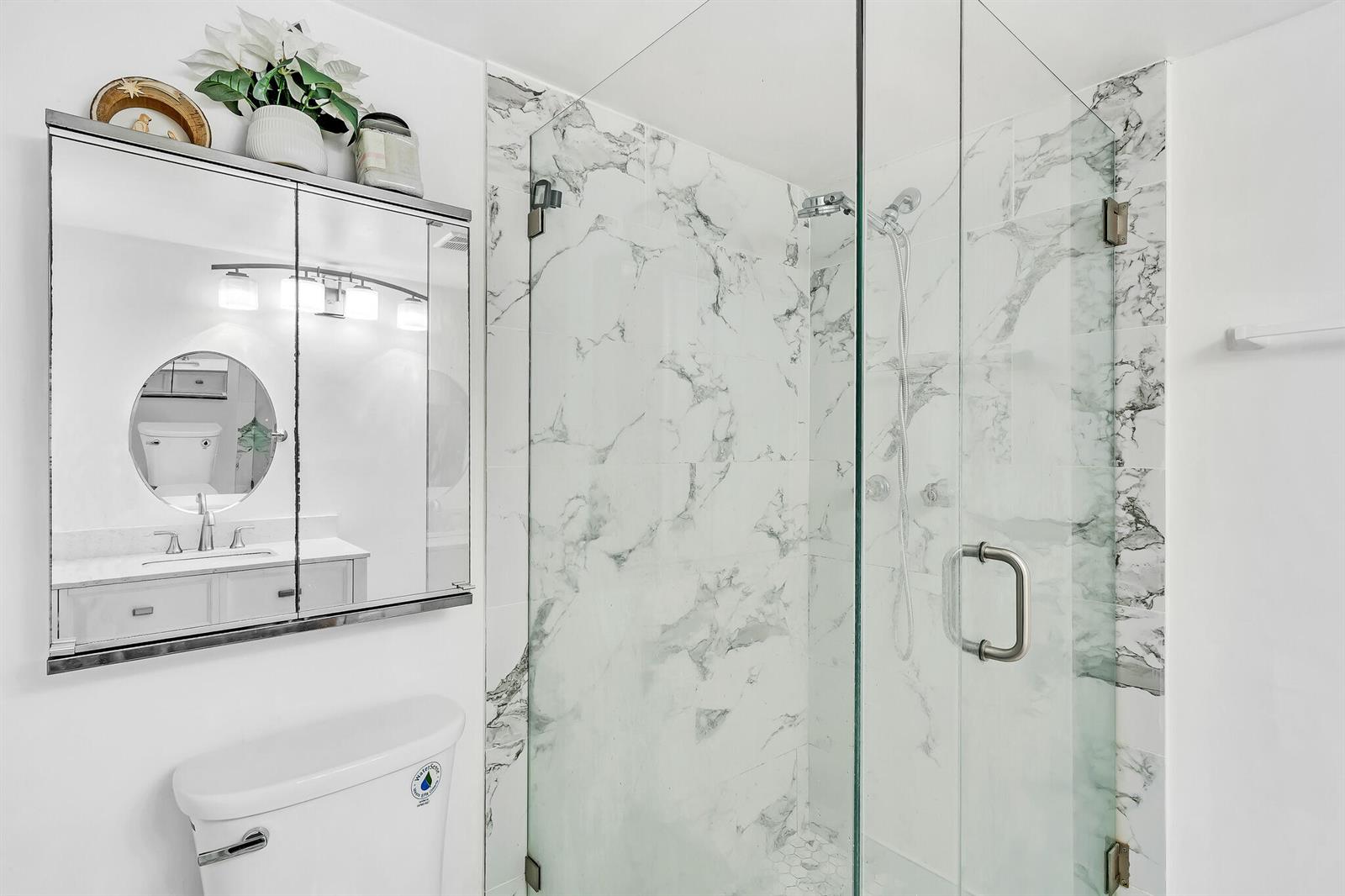 A bathroom features a glass-enclosed shower with marble-look tile, a toilet, and a mirrored medicine cabinet — 5940 NW 64th Avenue Unit 101, Tamarac FL 33319, TAMARAC, FL