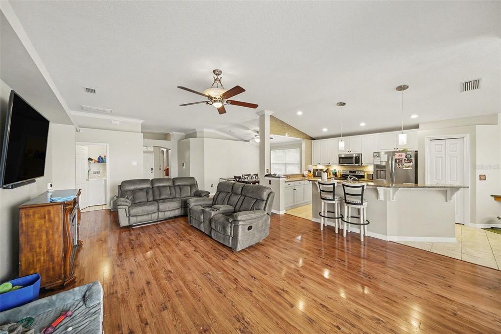 An open-concept living room and kitchen featuring wood flooring, gray sofas, and a breakfast bar — 215 FERN GULLEY DRIVE, SEFFNER, FL