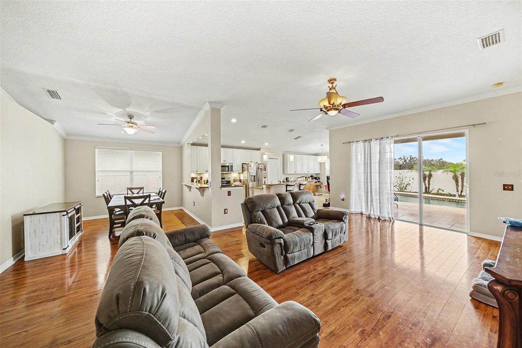 An open-concept living and dining area features hardwood floors, gray reclining furniture, and a kitchen — 215 FERN GULLEY DRIVE, SEFFNER, FL