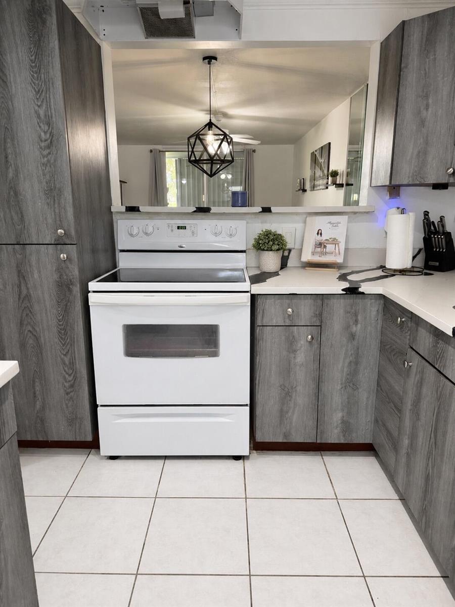 A kitchen features gray wood-grain cabinets, white appliances, and a pass-through window to another room — 5961 NW 2nd Avenue # 108, Boca Raton FL 33487, BOCA RATON, FL