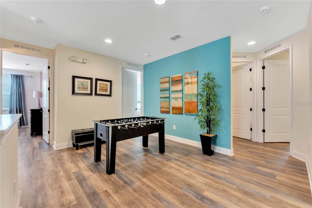 A game room features a foosball table, wood-look flooring, and a blue accent wall — 7517 MARKER AVENUE, KISSIMMEE, FL