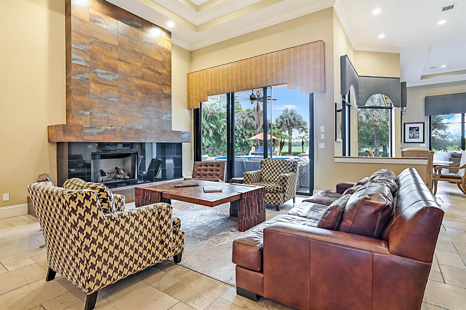 A living room features a large metal-tiled fireplace, leather sofa, patterned armchairs, and sliding glass doors — 18337 SE Old Trail Drive W, Jupiter FL 33478, JUPITER, FL
