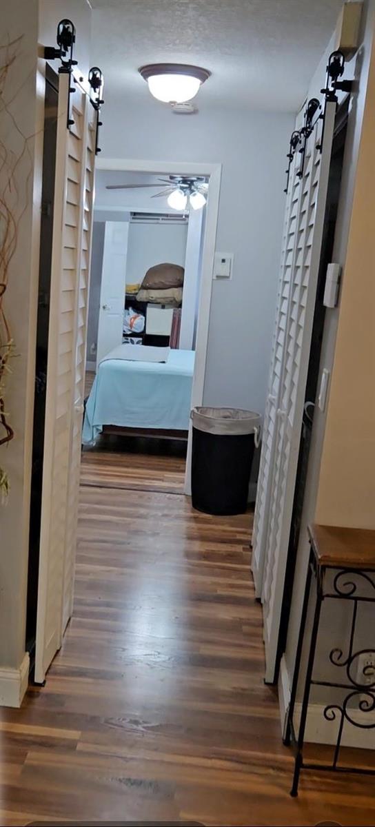 A hallway with wood-look flooring leads to a bedroom featuring white louvered sliding barn doors — 9215 W Sunrise Boulevard, Plantation FL 33322, PLANTATION, FL