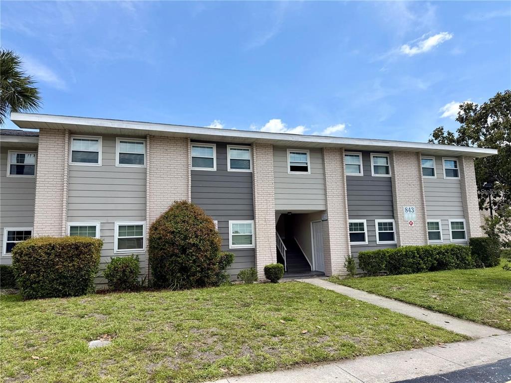 A two-story apartment building features light-colored brick, gray siding, and a central outdoor staircase — 843 SKY LAKE CIRCLE UNIT B, ORLANDO, FL