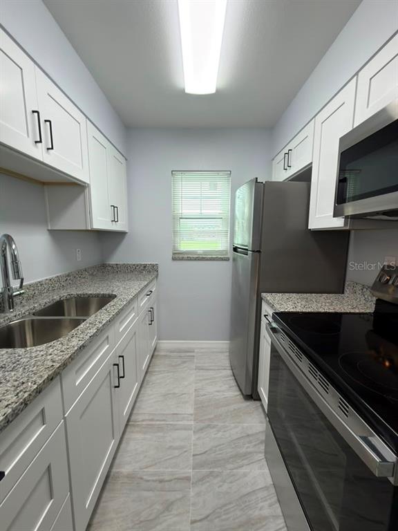 A galley kitchen features white cabinets, granite countertops, stainless steel appliances, and tile flooring — 843 SKY LAKE CIRCLE UNIT B, ORLANDO, FL