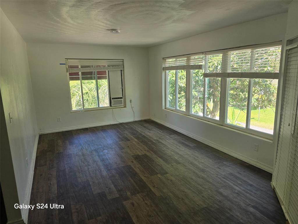 An empty room features wood-look flooring, white walls, and large windows with blinds — 7306 EARLWOOD AVENUE, MOUNT DORA, FL