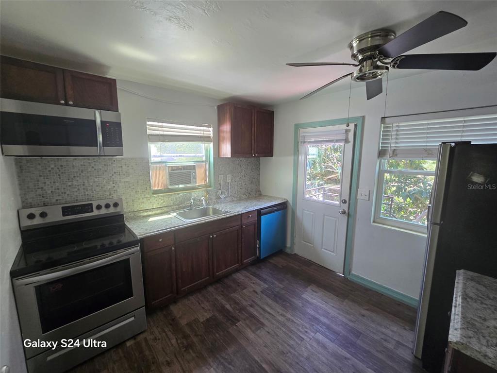 A kitchen features dark wood cabinets, stainless steel appliances, a tiled backsplash, and wood-look flooring — 7306 EARLWOOD AVENUE, MOUNT DORA, FL
