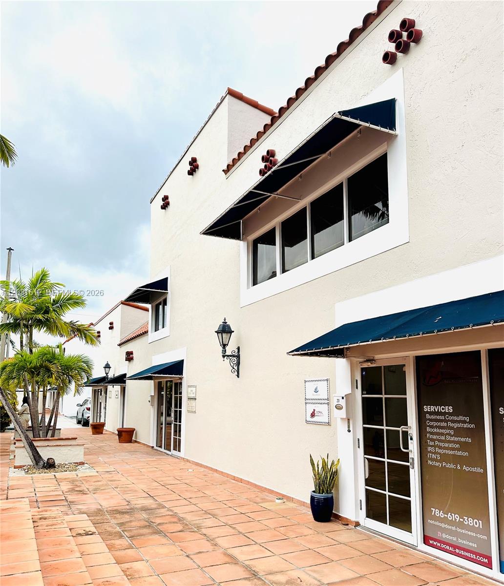 A low-angle exterior view shows a beige stucco building with blue awnings and a tiled walkway — DORAL, FL