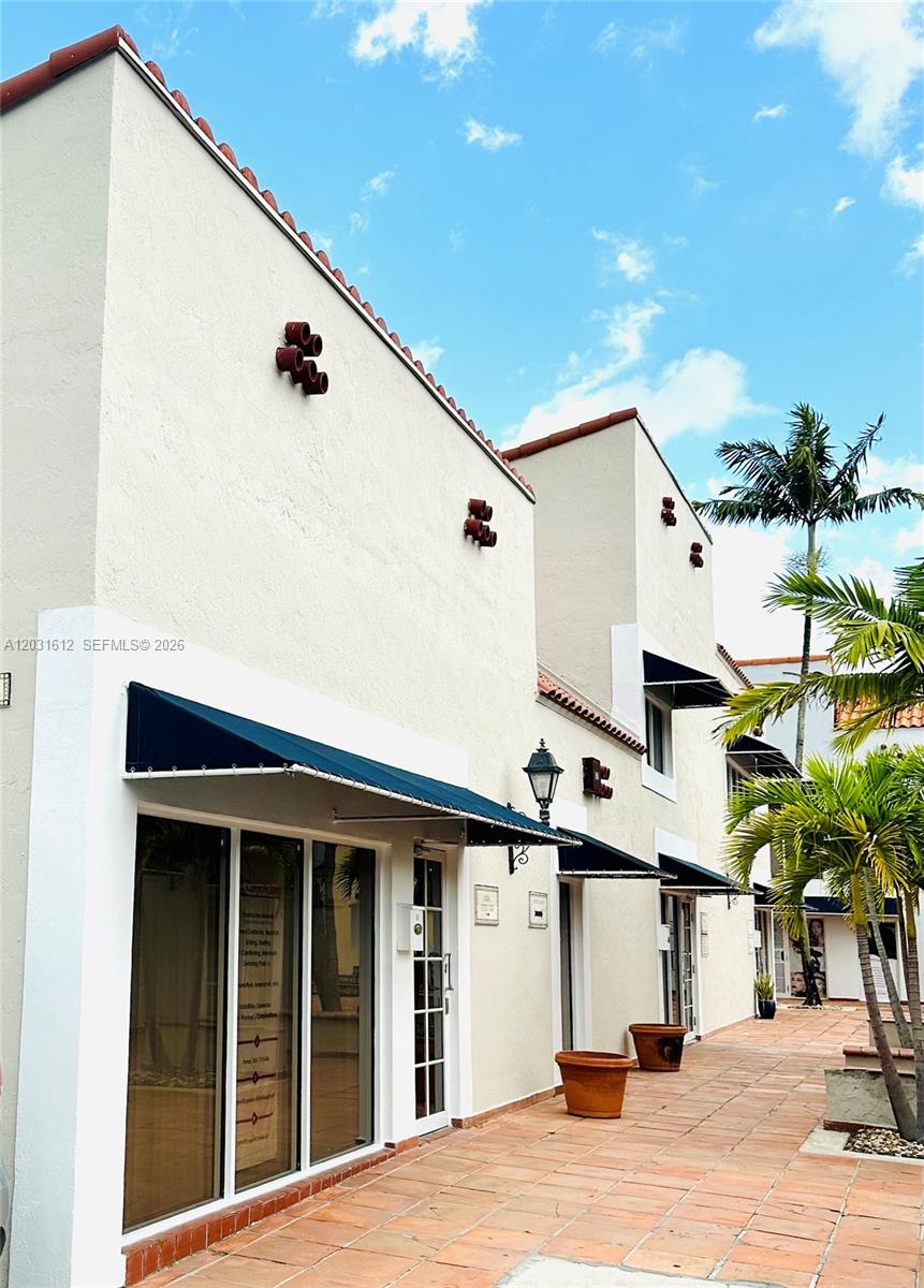 The exterior of a two-story stucco building features dark blue awnings and terracotta tile flooring — DORAL, FL