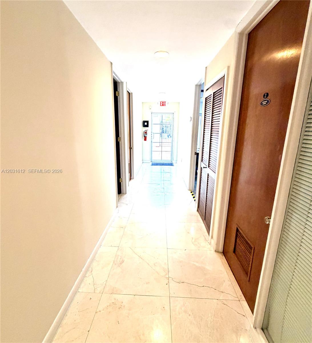 A tiled hallway leads to an exterior door with an exit sign above it — DORAL, FL