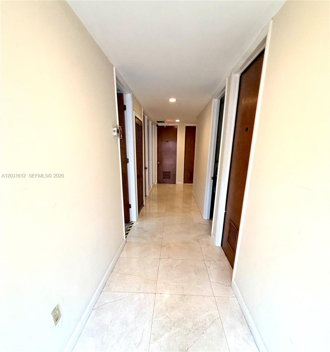 A narrow hallway features light-colored tile flooring, beige walls, and several dark wood doors — DORAL, FL