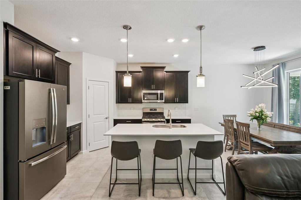 A kitchen features dark cabinets, a white island with bar stools, and a dining area — 1235 DORA PARC LANE, MOUNT DORA, FL