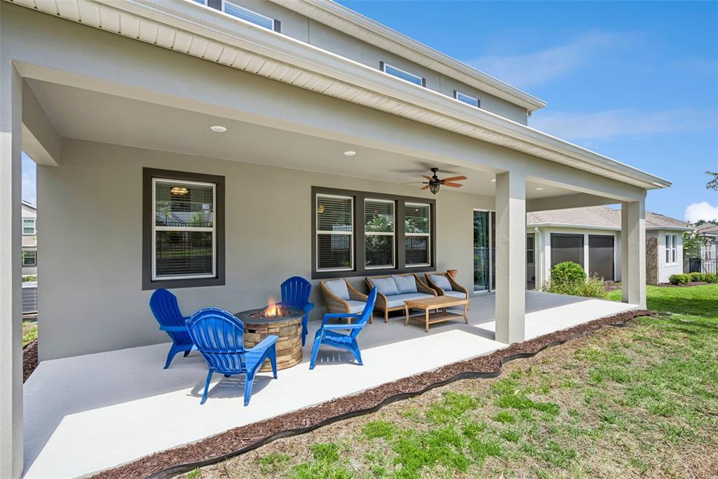 A covered concrete patio features blue Adirondack chairs, a fire pit, and outdoor seating — 1235 DORA PARC LANE, MOUNT DORA, FL