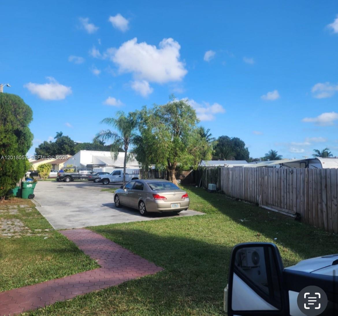 A paved driveway leads to a parked sedan in a yard with a wooden fence — 19422 SW 119th Ct, Miami FL 33177, MIAMI, FL