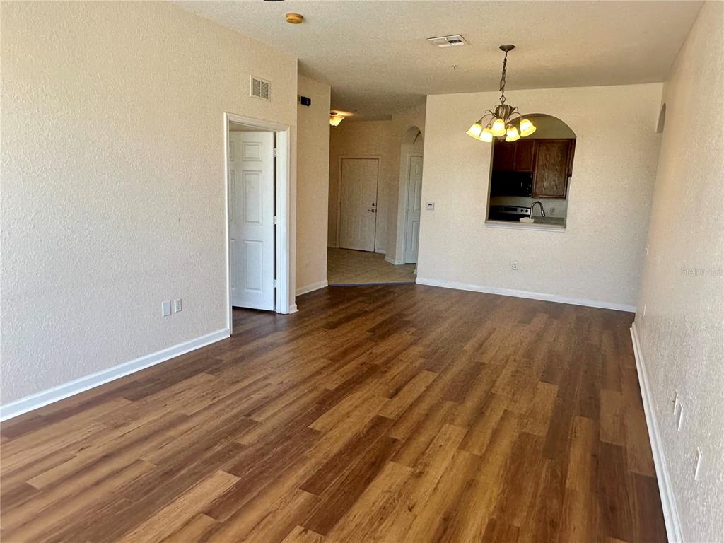 An open living area features wood-look flooring, a dining chandelier, and a kitchen pass-through window — 6402 CAVA ALTA DRIVE UNIT 410, ORLANDO, FL