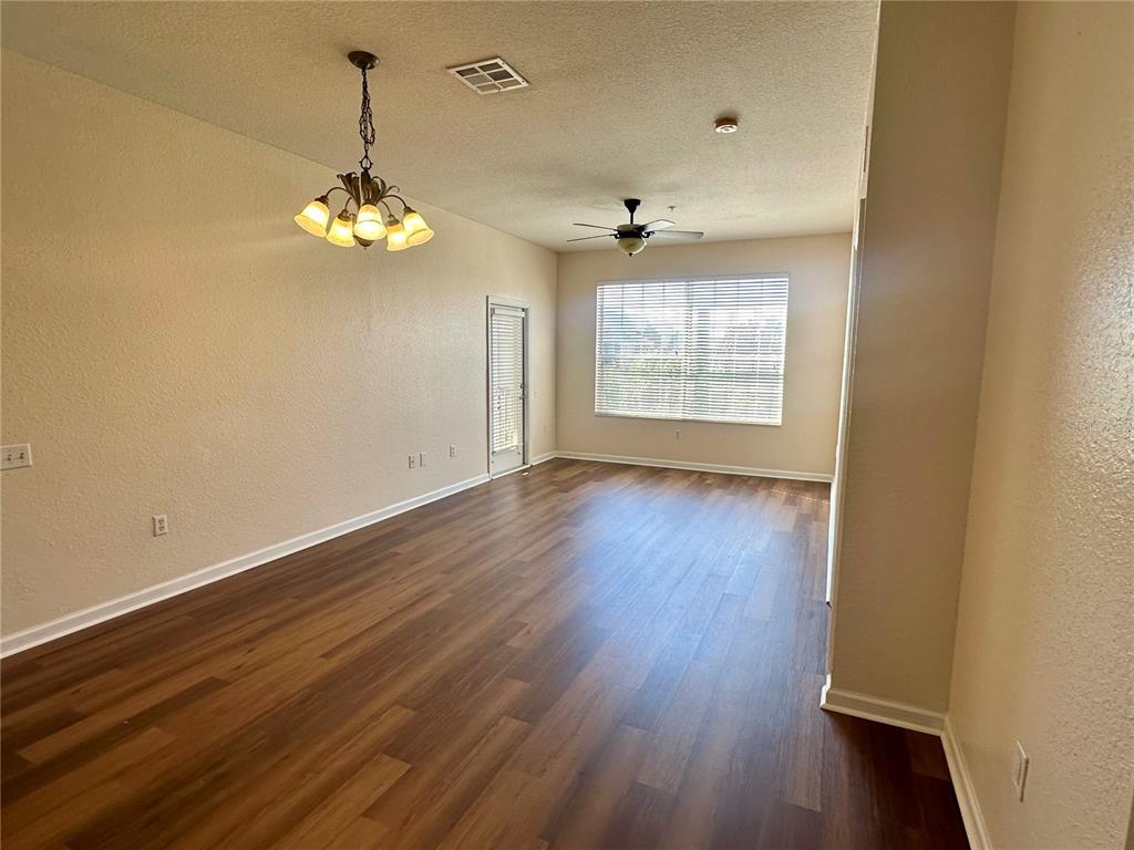 An empty room features wood-look flooring, a ceiling fan, a chandelier, and a glass door — 6402 CAVA ALTA DRIVE UNIT 410, ORLANDO, FL