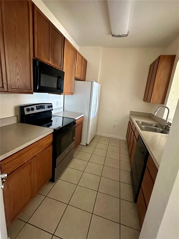 A kitchen features wood cabinets, stainless steel appliances, tile flooring, and a white refrigerator — 6402 CAVA ALTA DRIVE UNIT 410, ORLANDO, FL