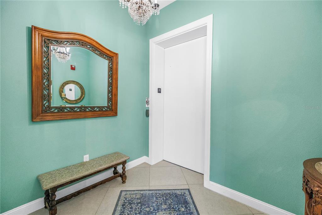 An entryway features a white elevator door, a decorative mirror, a bench, and teal walls — 10 FRANKLIN COURT S UNIT 63D, ST PETERSBURG, FL