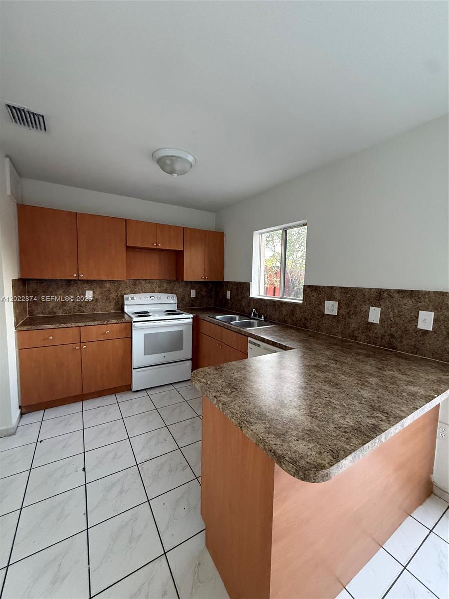A kitchen features wood cabinets, laminate countertops, white appliances, and white tile flooring — 18615 NW 84th Pl # 1, Hialeah FL 33015, HIALEAH, FL