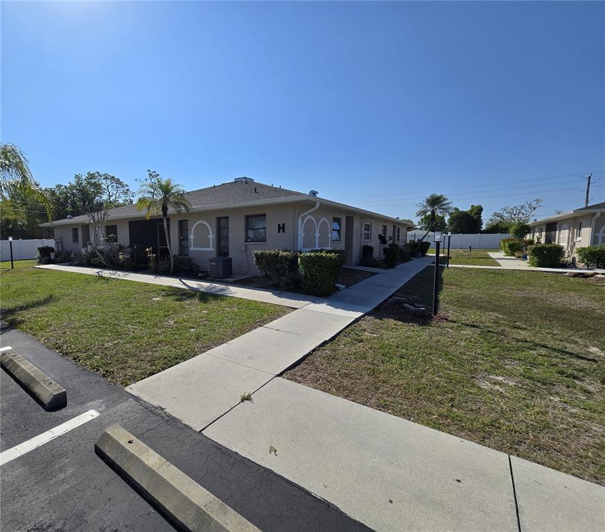 A single-story apartment building with a beige exterior and a sidewalk leading to entrances — 24540 HARBORVIEW ROAD UNIT H2, PUNTA GORDA, FL