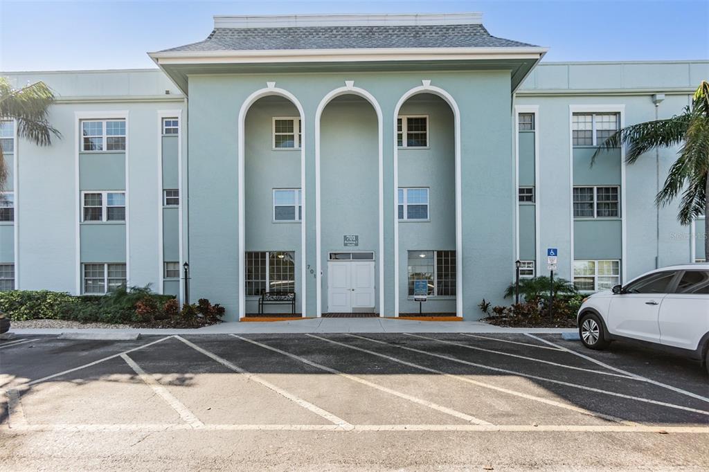 The exterior of a three-story light blue apartment building features three arched entryways — 701 POINSETTIA ROAD UNIT 306, BELLEAIR, FL