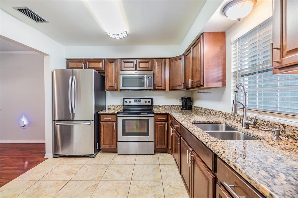 A kitchen features stainless steel appliances, dark wood cabinets, and granite countertops with tile flooring — 701 POINSETTIA ROAD UNIT 306, BELLEAIR, FL