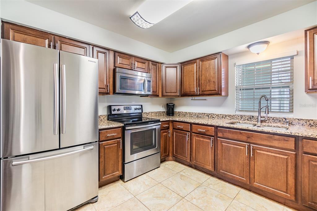 A kitchen with stainless steel appliances, dark wood cabinets, and granite countertops — 701 POINSETTIA ROAD UNIT 306, BELLEAIR, FL