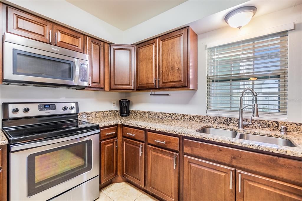 A kitchen features dark wood cabinets, granite countertops, stainless steel appliances, and a window above the sink — 701 POINSETTIA ROAD UNIT 306, BELLEAIR, FL