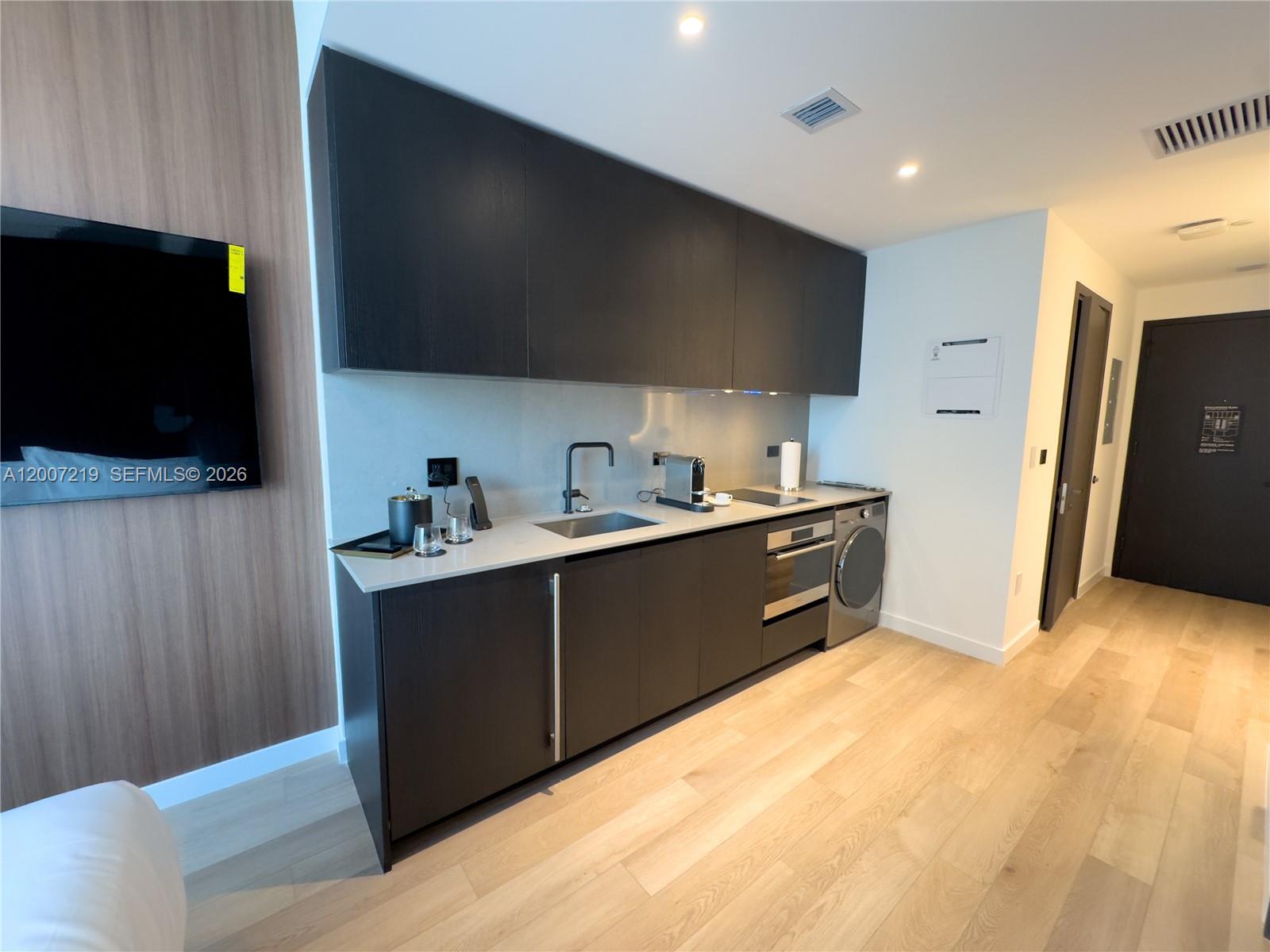 A modern kitchenette features dark cabinetry, light countertops, a sink, and an integrated laundry unit — 20 NE 11th St # 3006B, Miami FL 33132, MIAMI, FL