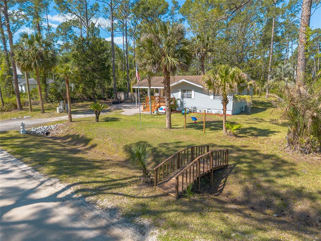 A light-colored house with a wooden bridge in the front yard and palm trees — 1650 11TH AVENUE, DELAND, FL