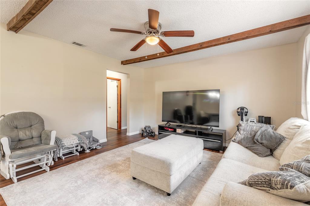 A living room features a ceiling fan, exposed wood beams, a television, and an ottoman — 1650 11TH AVENUE, DELAND, FL