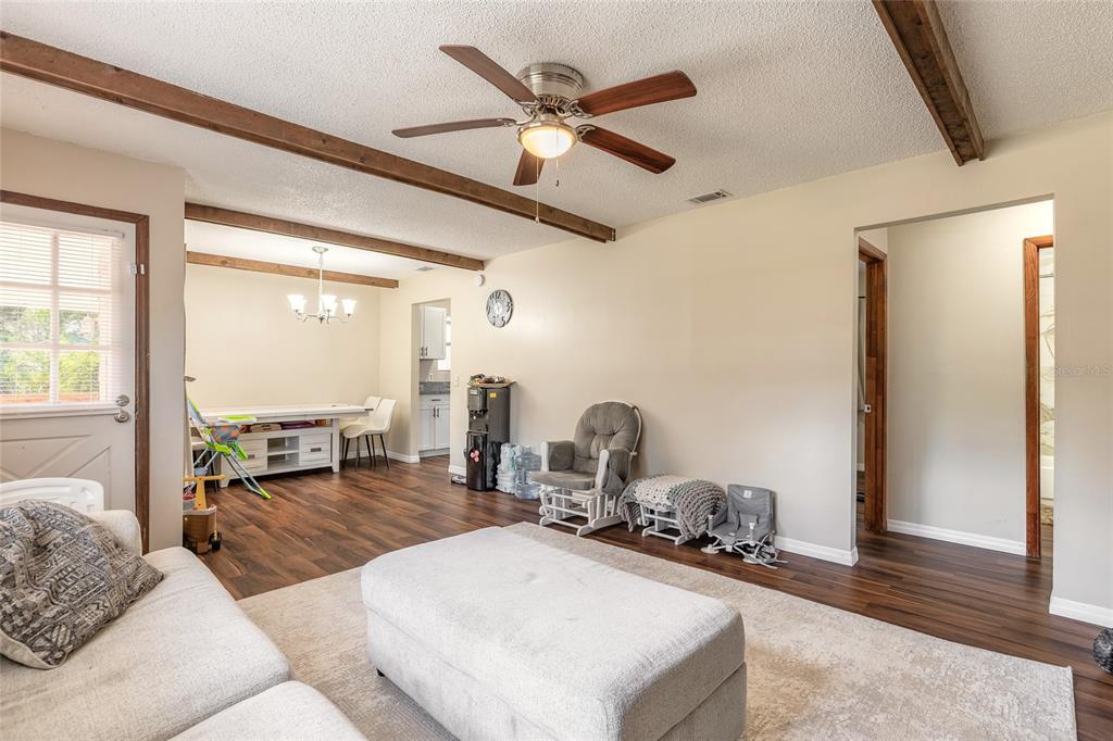 A living room with wood-look flooring, exposed ceiling beams, a ceiling fan, and an ottoman — 1650 11TH AVENUE, DELAND, FL