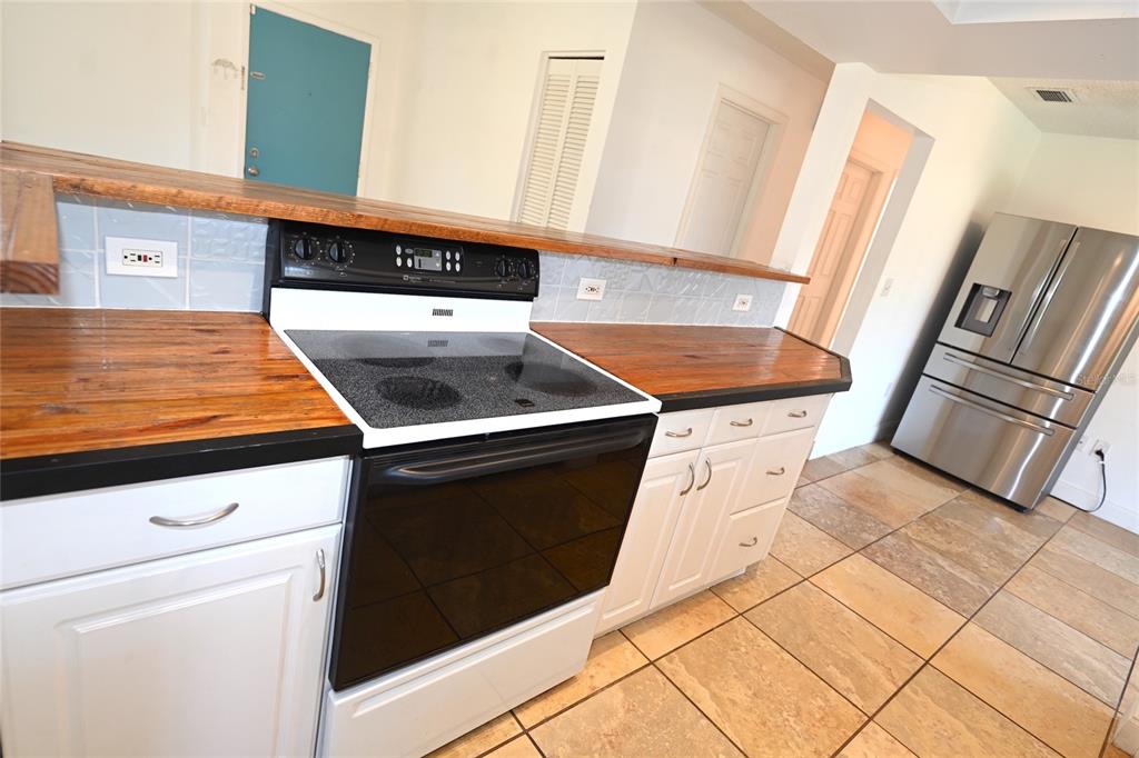 A kitchen features white cabinets, wood countertops, a glass-top stove, and stainless steel appliances — 6524 MAUNA LOA BOULEVARD, SARASOTA, FL