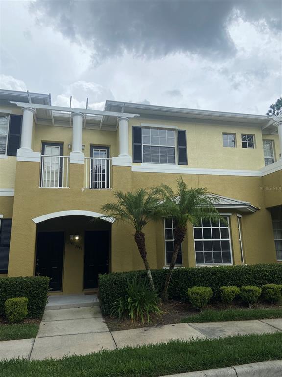 A two-story yellow stucco townhouse features a covered entryway, a second-floor balcony, and palm trees — 7441 ARLINGTON GROVE CIRCLE, TAMPA, FL