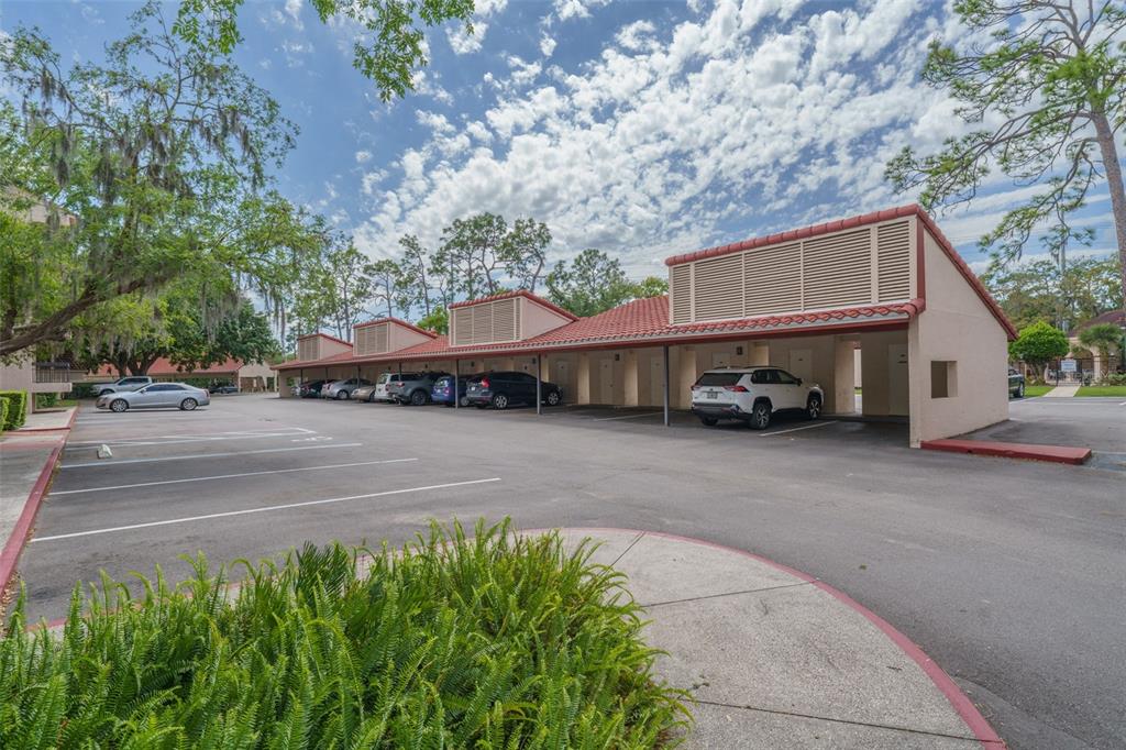 A row of covered parking spaces with a tiled roof sits beside an asphalt lot — 1150 CARMEL CIRCLE UNIT 302, CASSELBERRY, FL