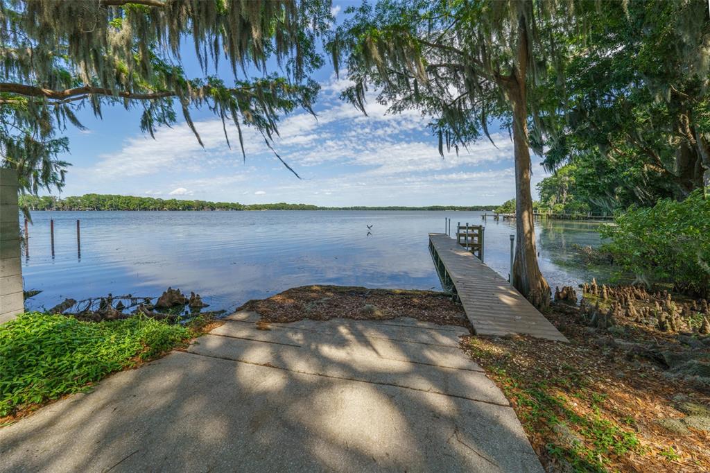 A concrete boat ramp leads to a wooden dock on a lake under mossy trees — 1150 CARMEL CIRCLE UNIT 302, CASSELBERRY, FL