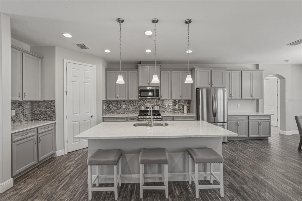 A kitchen features gray cabinets, a white quartz island with three stools, and wood-look flooring — 14633 RED CASTLE AVENUE, LITHIA, FL