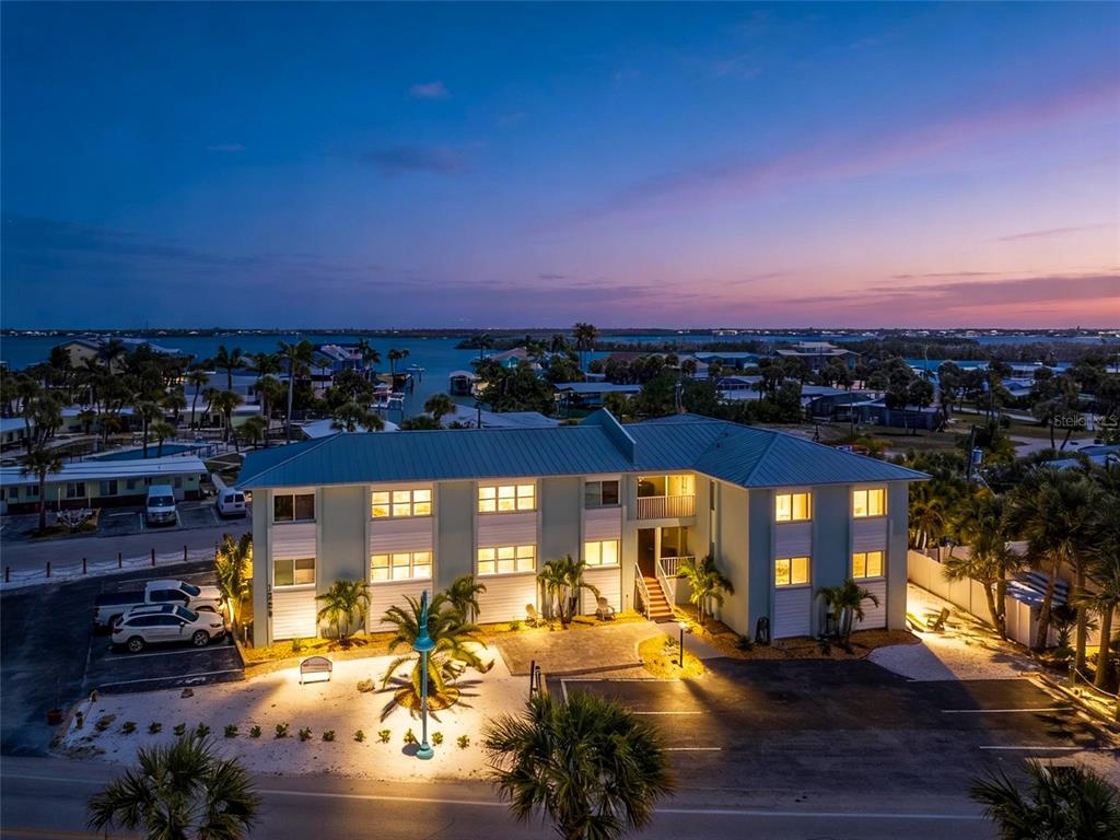 An aerial view of a multi-story coastal apartment building at dusk with parking and palm trees — 1285 GULF BOULEVARD UNIT 4, ENGLEWOOD, FL