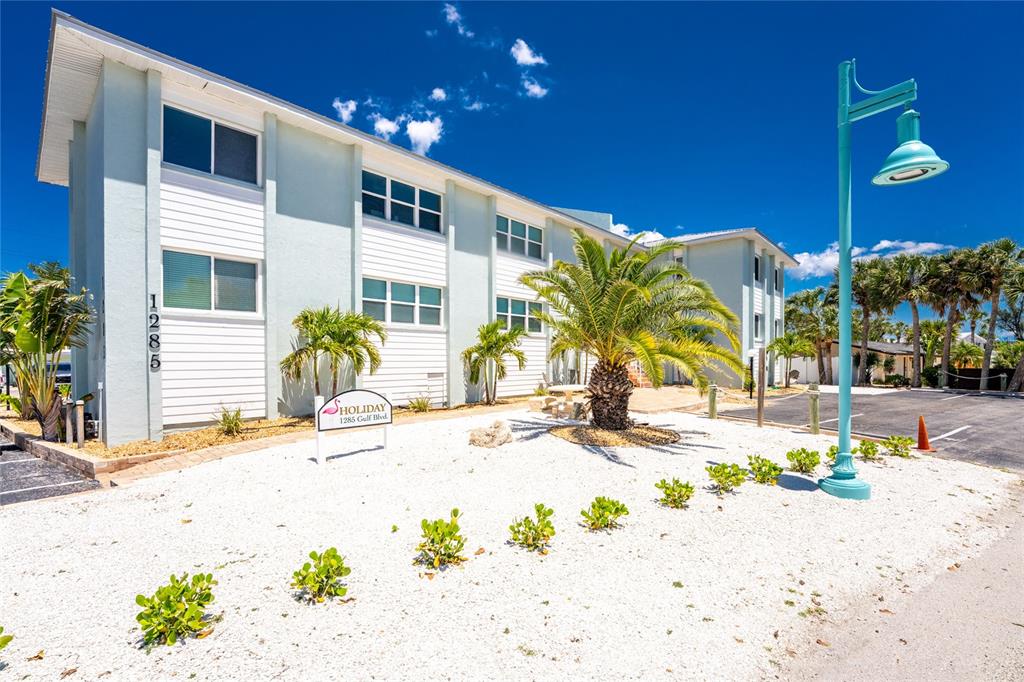 A two-story light blue apartment building features white trim, palm trees, and a gravel yard — 1285 GULF BOULEVARD UNIT 4, ENGLEWOOD, FL